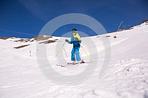 Little girl in blue and yellow ski costume skiing in downhill slope. Winter sport recreational activity