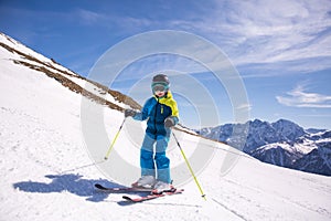 Little girl in blue and yellow ski costume skiing in downhill slope. Winter sport recreational activity