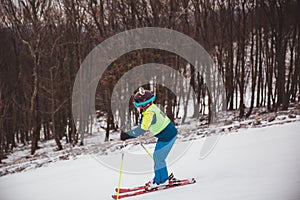 Little girl in blue and yellow ski costume skiing in downhill slope. Winter sport recreational activity