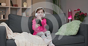 Little girl in bluetooth headphones enjoying music with mp3 player on smartphone, singing along to her favorite song