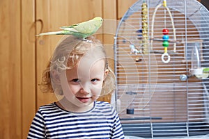 A little girl with a boogie on her head next to a large cage in the living room.