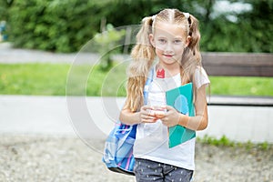 Little girl with book and backpack in school park. The concept of school, study, education, friendship, childhood