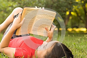 Little girl with a book in the garden. Kid is readding a book on hands. outdoors in summer day. Countryside