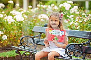 Little girl with a book in her hands in the park outdoors
