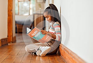 Little girl, book and reading on wooden floor for learning, education or story time relaxing at home with smile. Happy