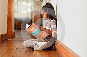 Little girl, book and reading on wooden floor for story time, learning or education relaxing at home with smile. Happy