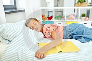 Little girl with book sleeping in her room at home