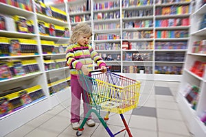 Little girl in bookshop, with cart for purchases