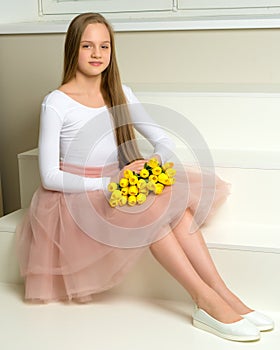 A little girl with a bouquet of tulips is sitting on the stairs.