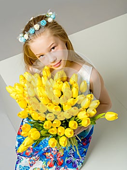 A little girl with a bouquet of tulips is sitting on the stairs.