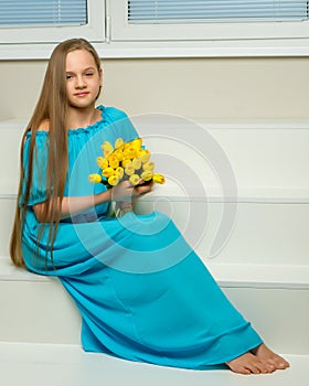 A little girl with a bouquet of tulips is sitting on the stairs.