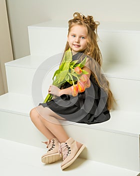 A little girl with a bouquet of tulips is sitting on the stairs.