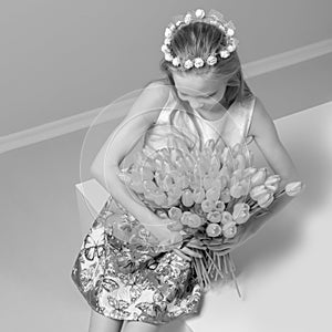 A little girl with a bouquet of tulips is sitting on the stairs.