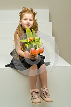 A little girl with a bouquet of tulips is sitting on the stairs.