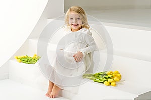 A little girl with a bouquet of tulips is sitting on the stairs.