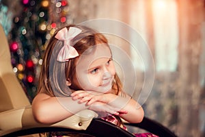 Little girl with bow at the Christmas tree sitting