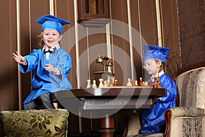 Little girl and boy in blue suits play chess