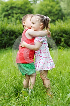 Little girl and boy embrace on fresh green grass photo