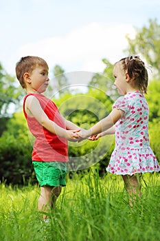 Little girl and boy hold hands on fresh green