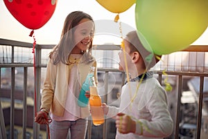 Little girl and boy holding balloons and spending a wonderful time together on the terrace of an apartment. Family, together,