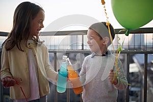 Little girl and boy holding balloons and toasting on the terrace of an apartment. Family, together, party