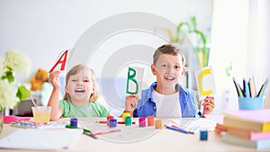 A little girl and a boy learn at home. happy kids at the table with school supplies smiling funny and learning the alphabet in a