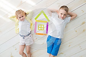 A little girl with a boy lie on the floor next to a house of colored paper. View from above