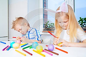 Little girl and boy in rabbit bunny ears on head are preparing for Easter and painting eggs. Colorful markers. Easter, family and