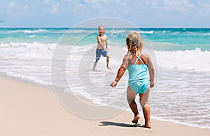 little girl and boy run play with waves on beach