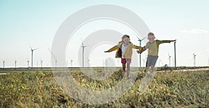 Little girl and boy are running in front of windmills. Renewable energies and sustainable resources - wind mills