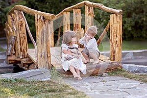 A little girl and a boy sit on a bridge across the river. A girl holds a pet rabbit in her hands.