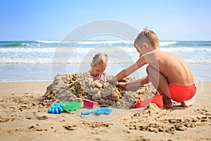 Little Girl Boy Sit near Heap Play at Wave Surf on Beach