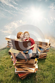 Little girl and boy sitting on the tower made of big books