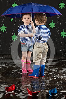 Little girl and boy under a blue umbrella hiding