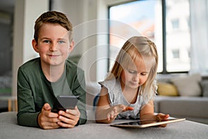 Little girl and boy watching video or playing games on their digital device tablet, smartphone.