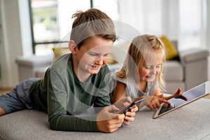 Little girl and boy watching video or playing games on their digital device tablet, smartphone.