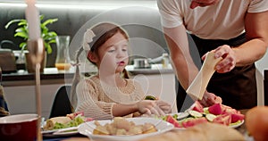 Little girl with braided hair tastes fresh vegetables at the dinner table and tells her dad to salt them with. A middle