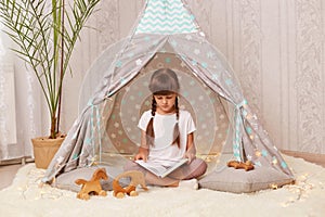 Little girl with braids wearing white t shirt posing in wigwam