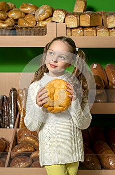 Little girl with bread in hand. bread's shelves background . S
