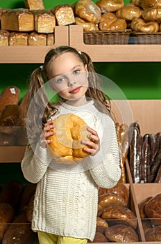 Little girl with bread in hand. bread`s  shelves  background . Supermarket or bread shop