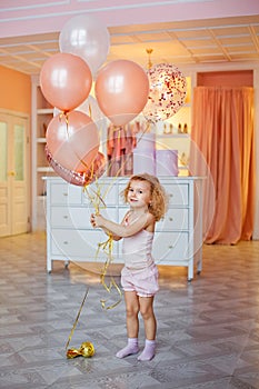 A little girl in a bright room in her pajamas. Baby with balloons, childhood concept, birthday party, surprise in the morning