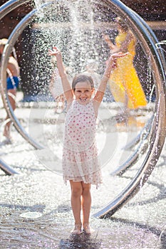 Little girl in a bright sundress rejoices drops of the city fountain