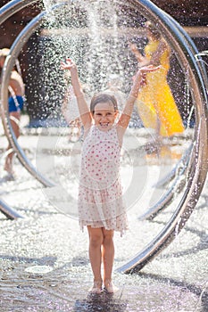 Little girl in a bright sundress rejoices drops of the city fountain photo