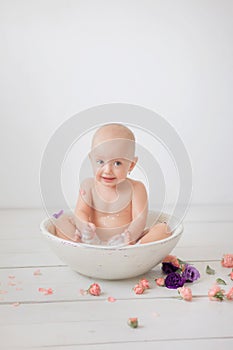 Little girl in a bright white room bathes in a white bowl with milk