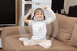 A little girl with a broken arm and a cast raises her arms up