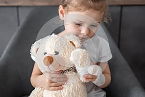 Little girl with broken finger holds teddy bear with a bandaged paw at the doctor& x27;s appointment in the hospital