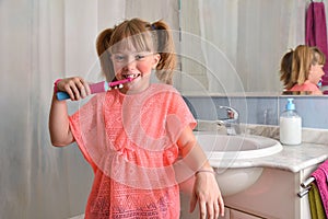 Little girl brushing her teeth with electric toothbrush in bathroom