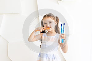 Little girl brushing her teeth on a white background and holding toothbrushes, place for text, healthy teeth