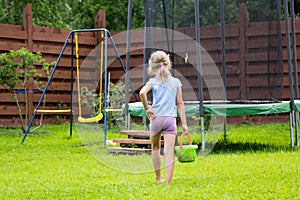 Little girl with bucket of water going to wash her trampoline