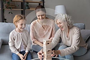 Little girl build tumbling tower with mom and old grandma